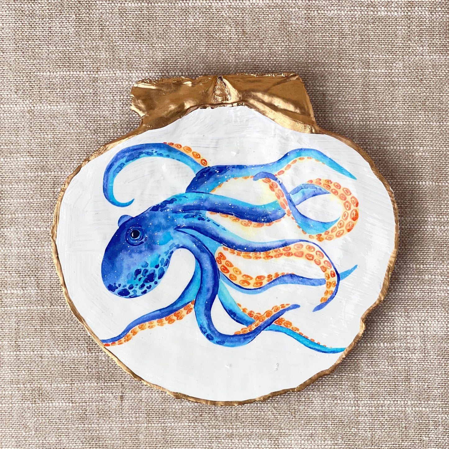 A decorative ring dish with a blue and orange octopus design, made from scallop shell with a white background.