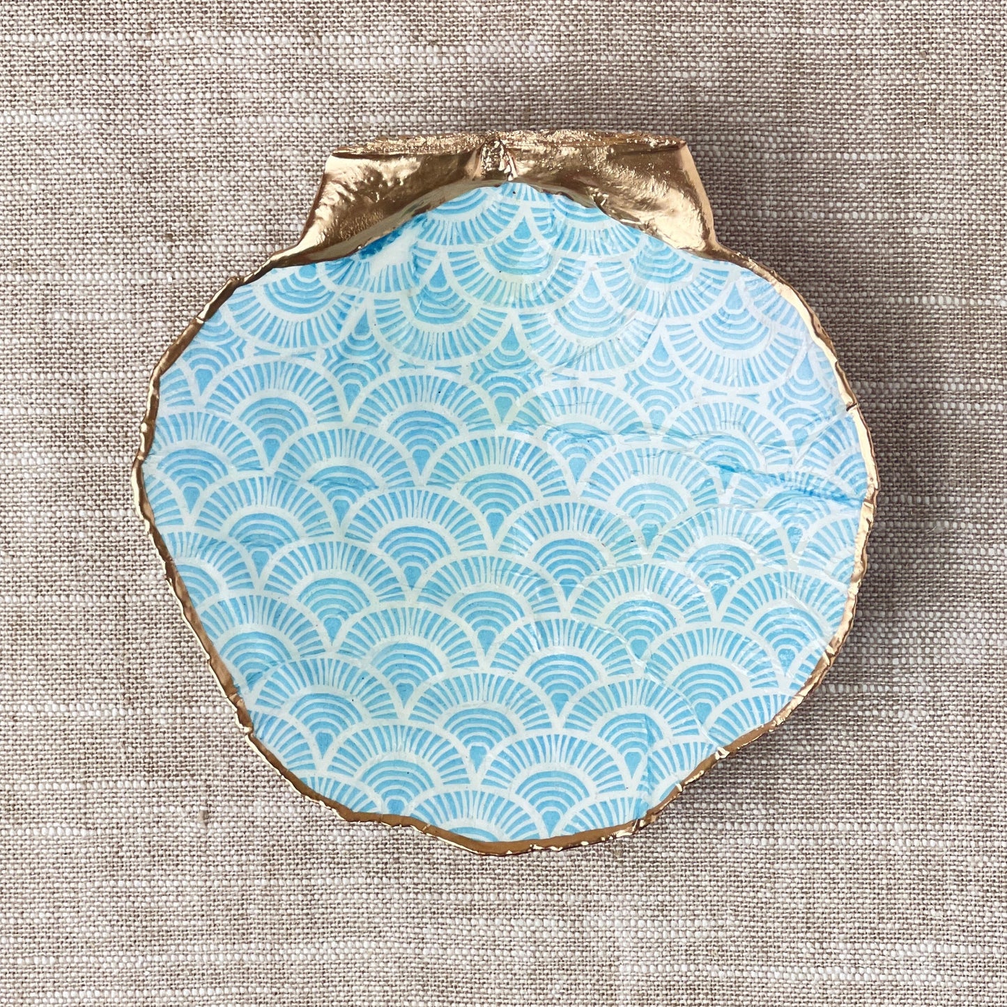 Decorative plate with blue wave pattern and gold rim on a textured surface