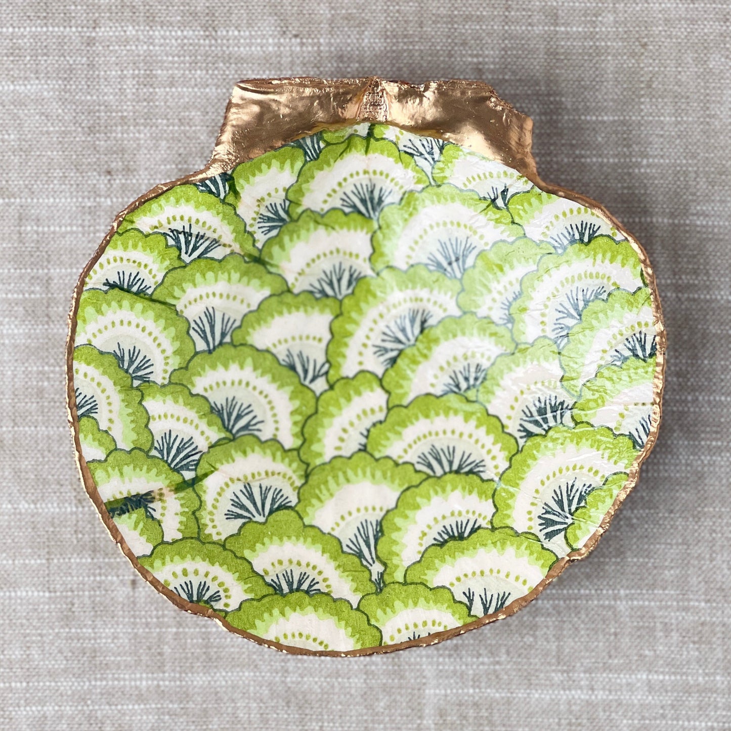 A scallop shell with a green floral fan print design, used as a ring dish.