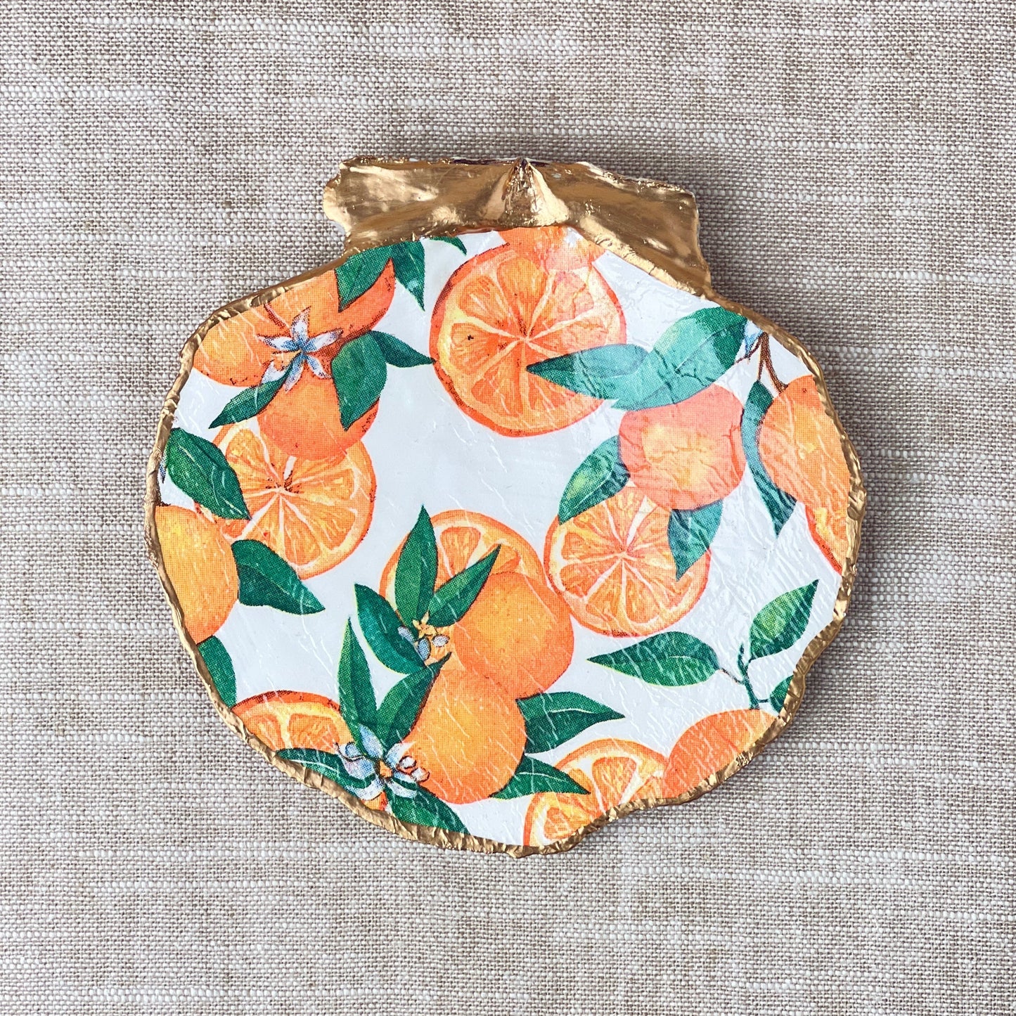 A scallop shell ring dish with an orange design, placed on a neutral background.