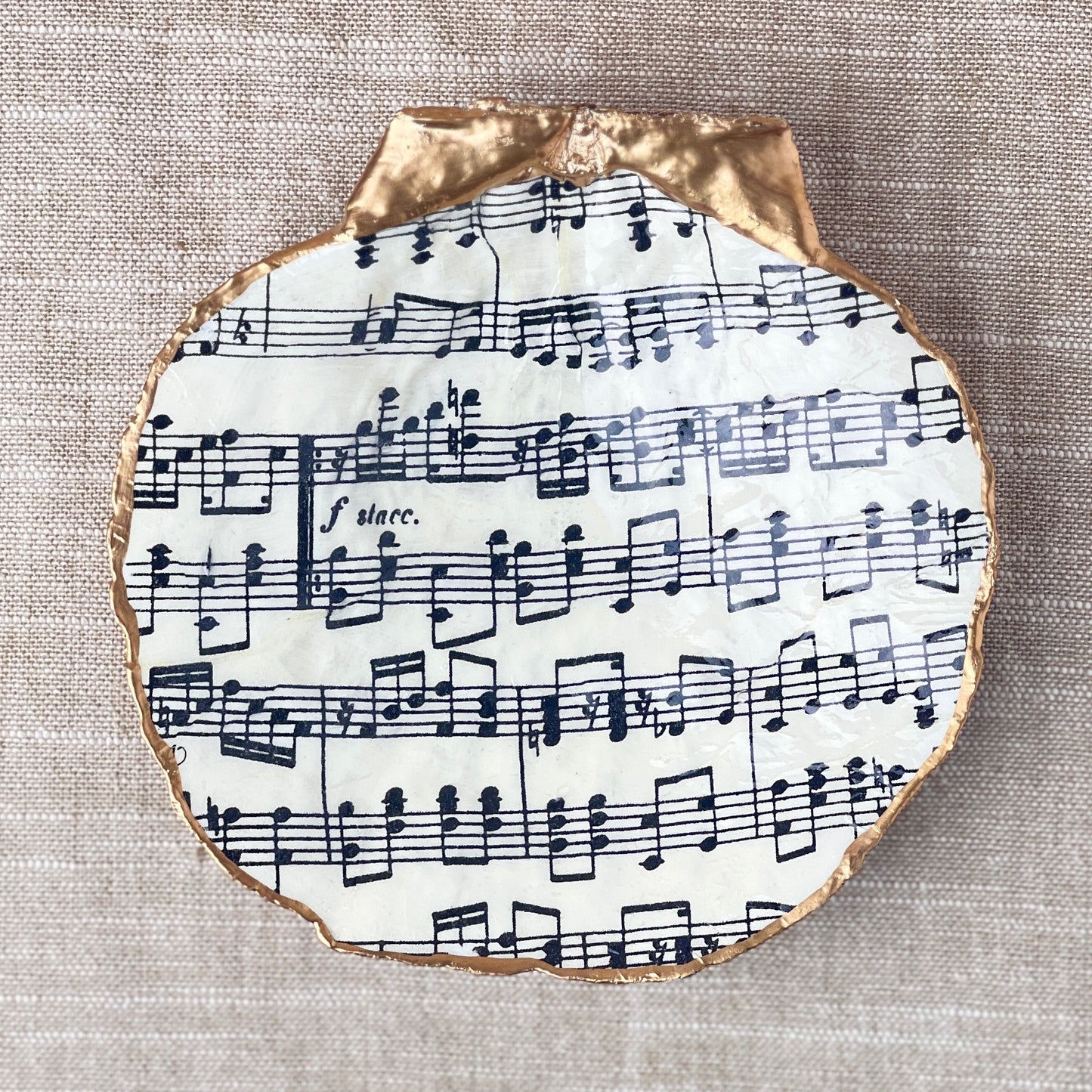 A scallop shell ring dish with a sheet music design, decorated and displayed on neutral background.