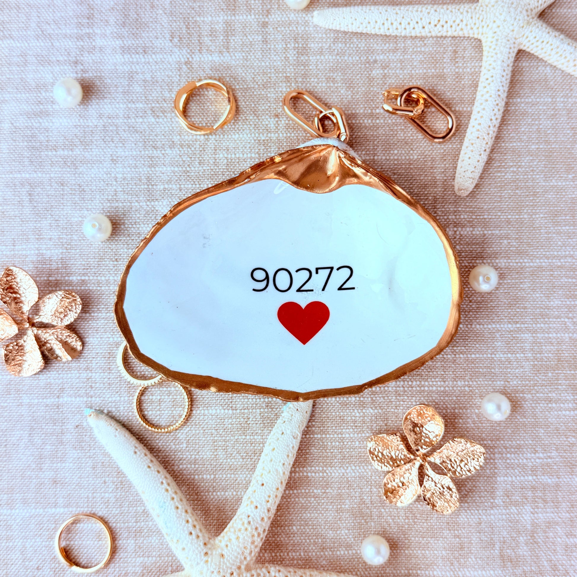 Decorative pendant with '90272' and a heart on a textured beige background with starfish and pearls.