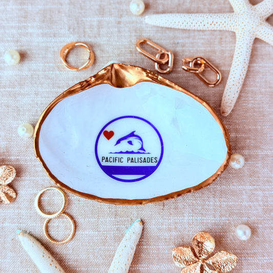 Medium clam shell with a Pacific Palisades logo on a white surface with starfish and pearls
