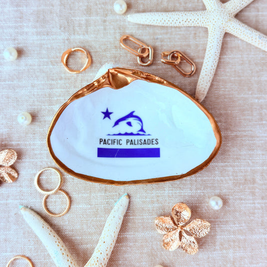 Shell-shaped dish with 'Pacific Palisades Flag' logo surrounded by starfish and pearls on a beige linen background