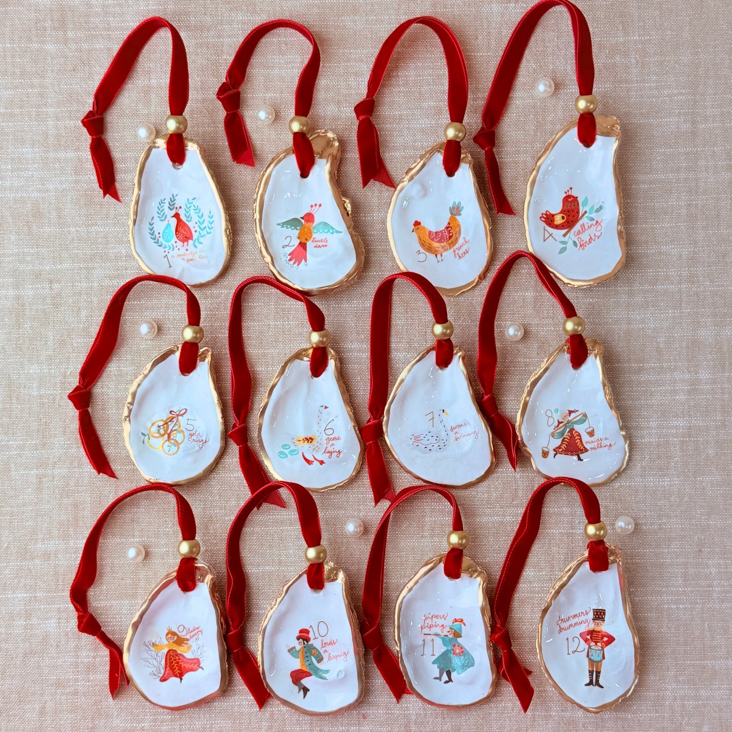 Set of decorative Christmas ornaments featuring 12 days of Christmas design with red ribbons on a beige fabric background