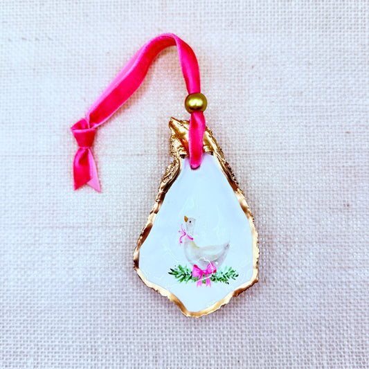 Decorative ornament with a gold edge, white center featuring a bird, and pink ribbon on a textured beige background.