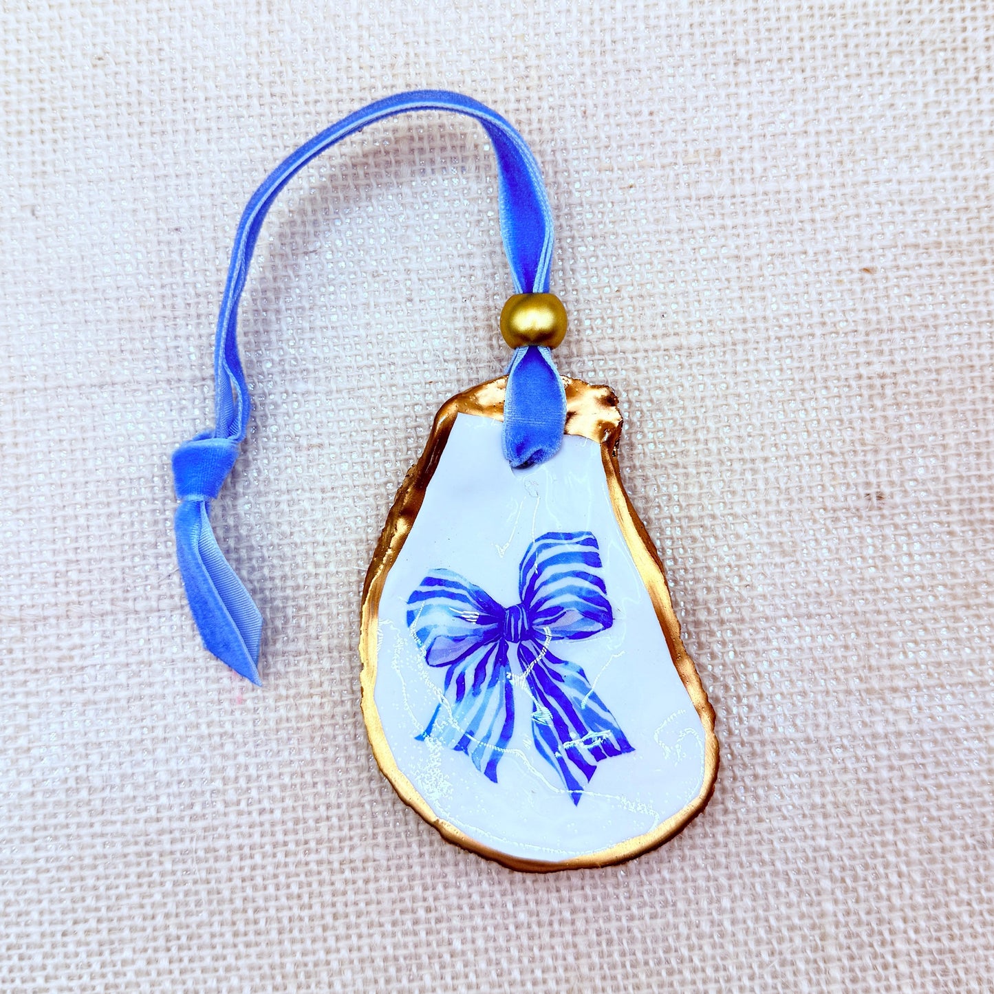 Decorative oyster ornament with blue bow design on a beige fabric background