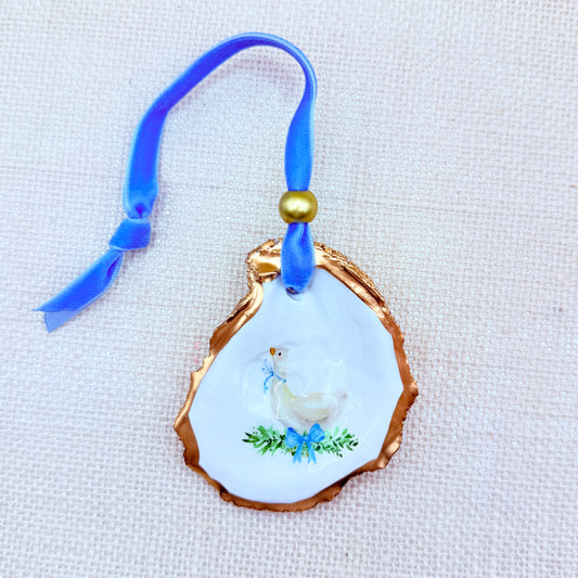 Decorative oyster ornament with a blue mother goose design and blue ribbon and gold accent on a textured beige background.