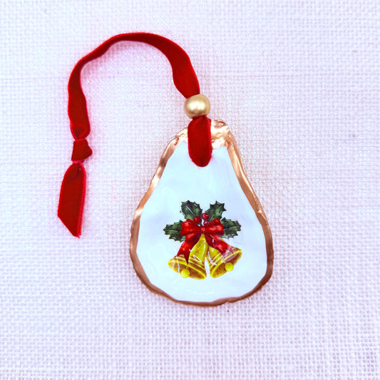 Christmas bells oyster ornament with red ribbon and holly design on a light background.