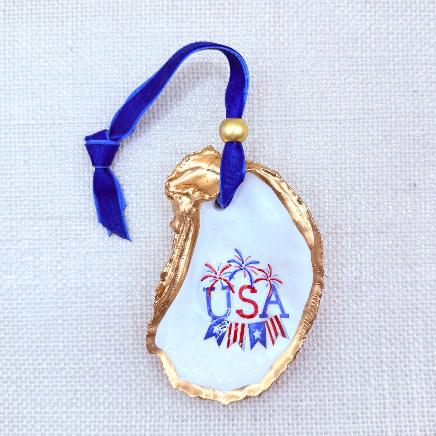 Decorative oyster ornament with 'USA' text and blue ribbon on a white background