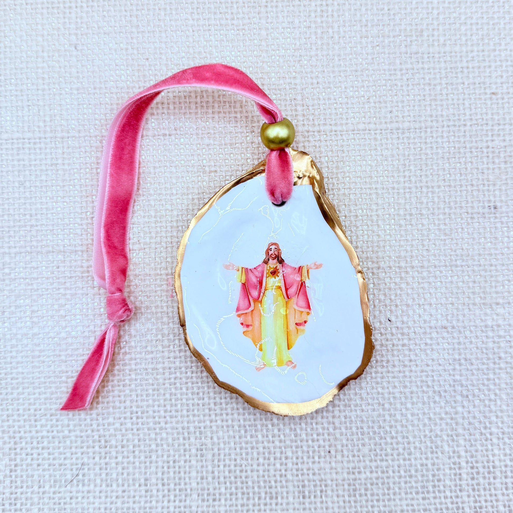Decorative ornament with a religious figure on a pink ribbon against a light background