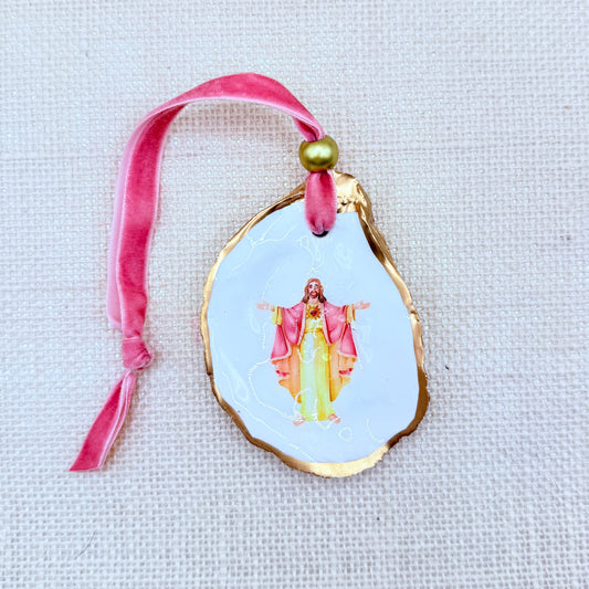 Decorative ornament with a religious figure on a pink ribbon against a light background