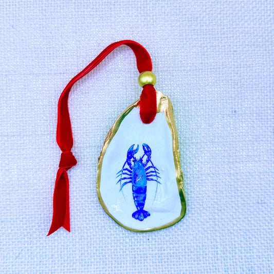 Decorative oyster shell with a blue lobster design on a red ribbon against a light fabric background