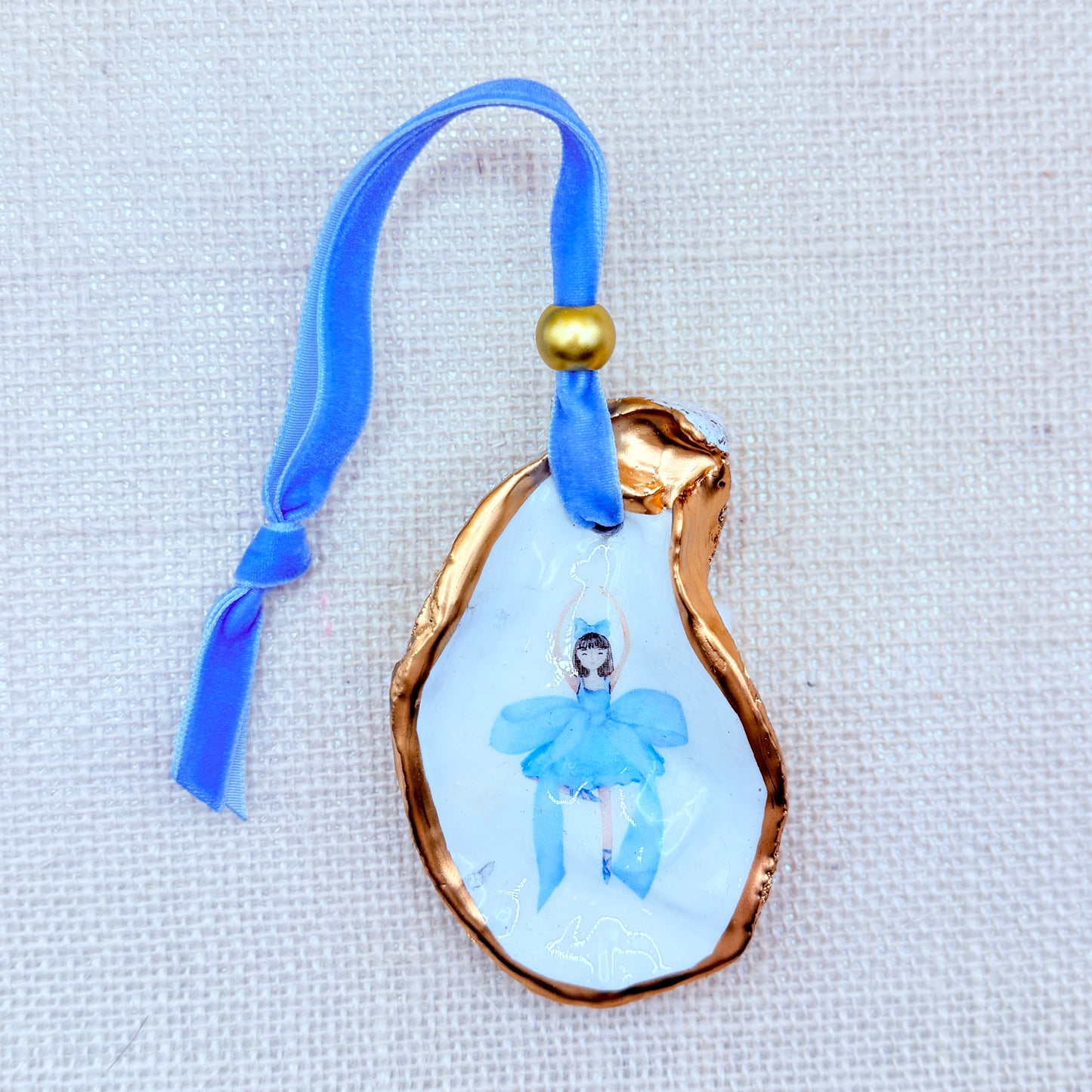 Decorative holiday ornament with a blue ribbon and gold accents on a textured white background.