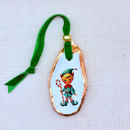 Decorative oyster ornament of an elf design and green ribbon on a light fabric background.