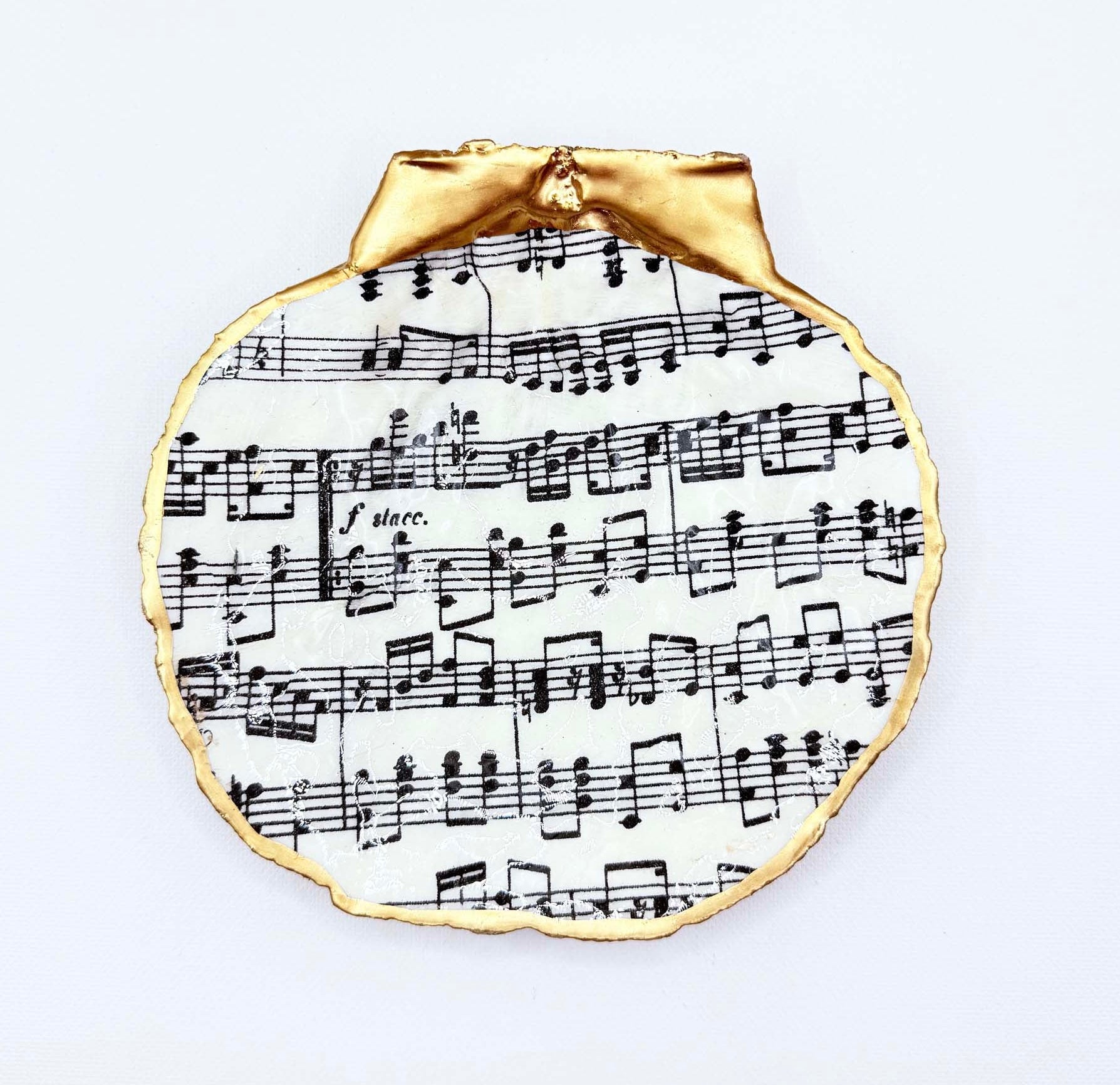 A scallop shell ring dish with a sheet music design displayed on white background.