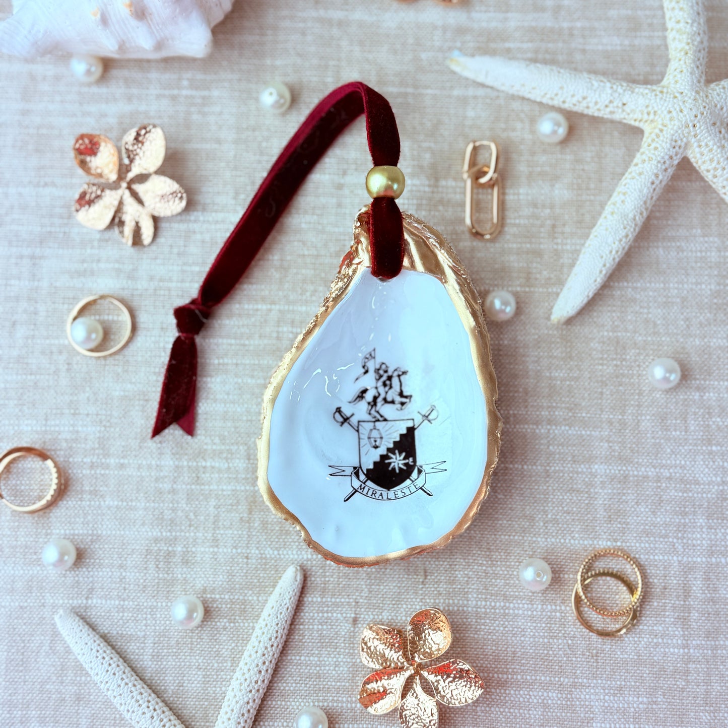 Decorative oyster shell with the Miraleste High School crest design on a textured surface with starfish and pearls.