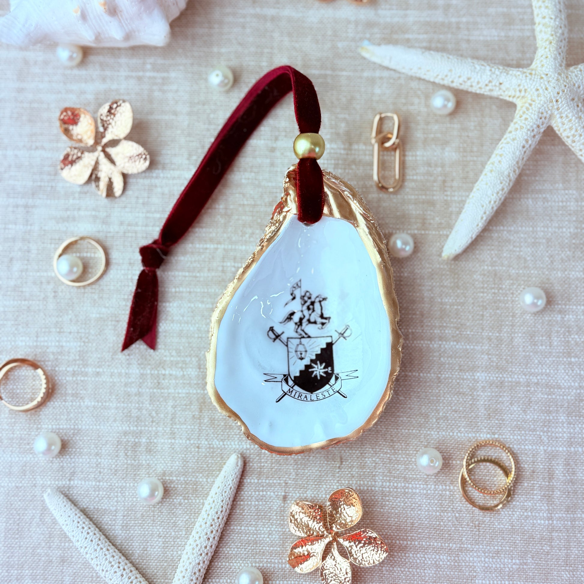 Decorative oyster shell with the Miraleste High School crest design on a textured surface with starfish and pearls.