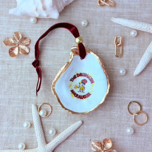 Decorative holiday ornament oyster shell with the drunken marauder from Miraleste High School on a textured surface with starfish and pearls.