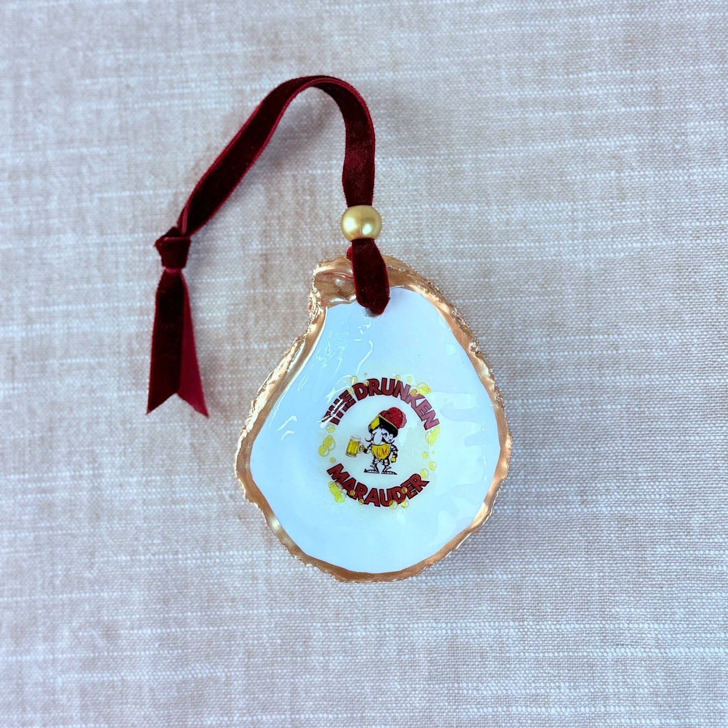 Decorative holiday ornament oyster shell with the drunken marauder from Miraleste High School on a textured surface.