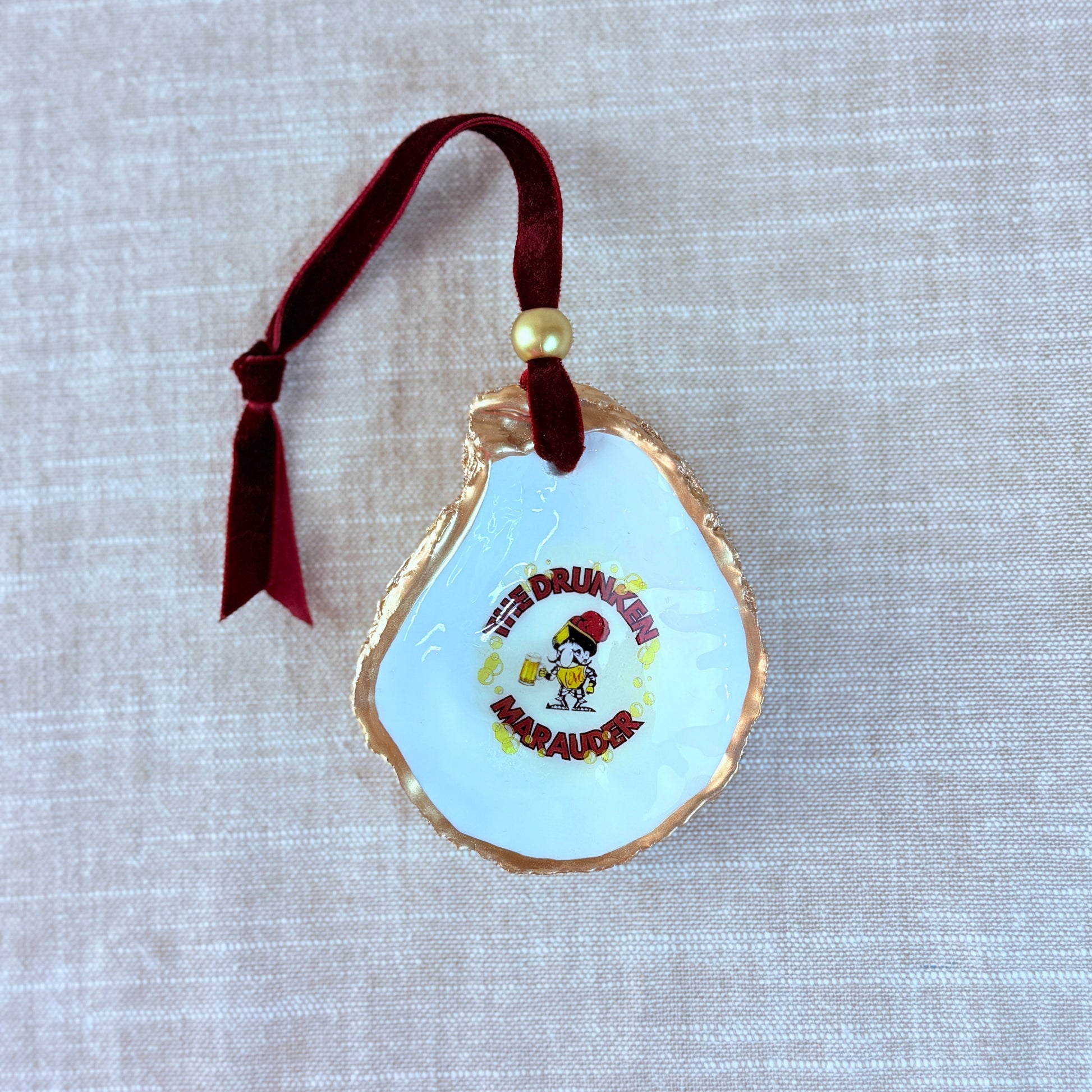 Decorative holiday ornament oyster shell with the drunken marauder from Miraleste High School on a textured surface.