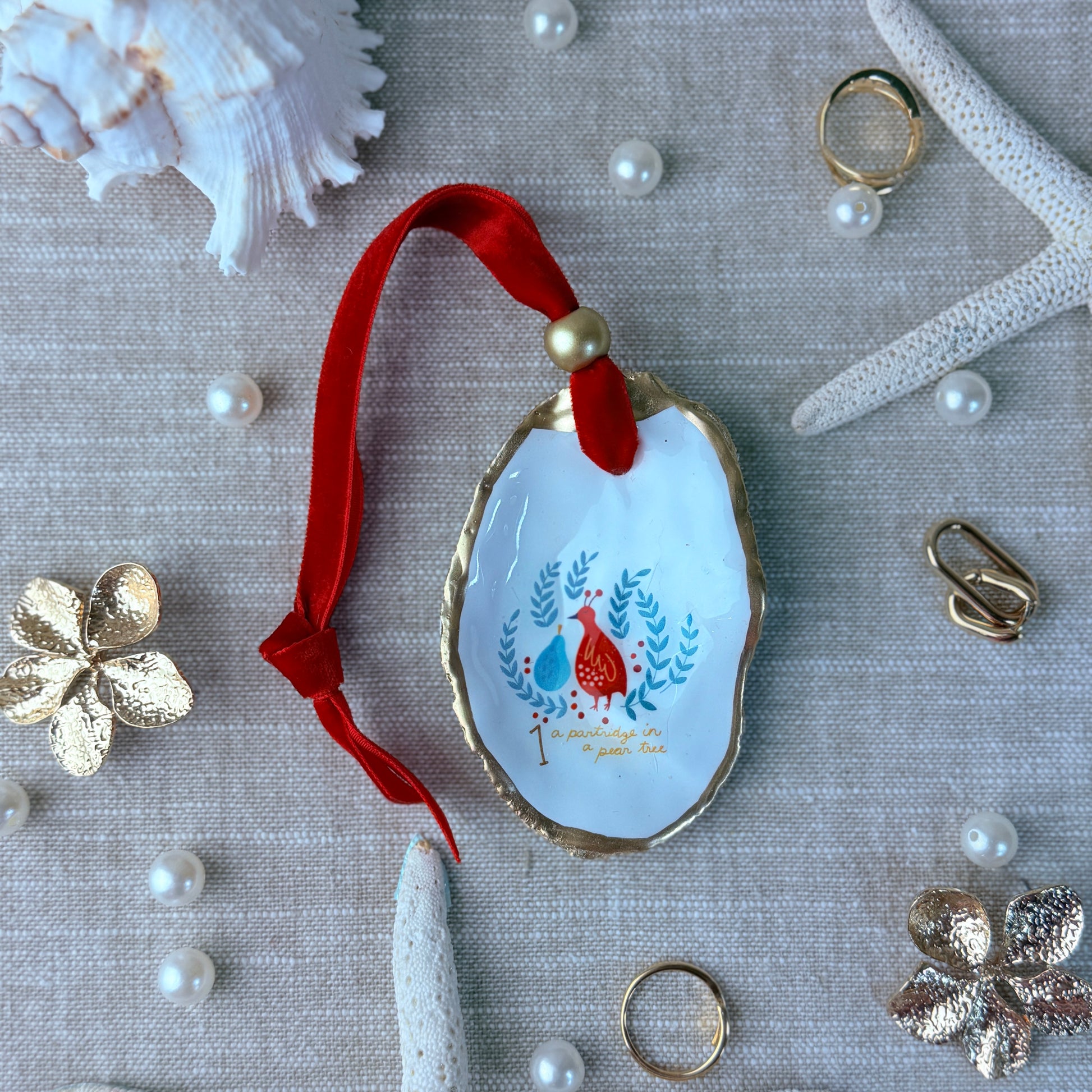 Decorative shell ornament with red ribbon and bird design on a textured surface with pearls and starfish.