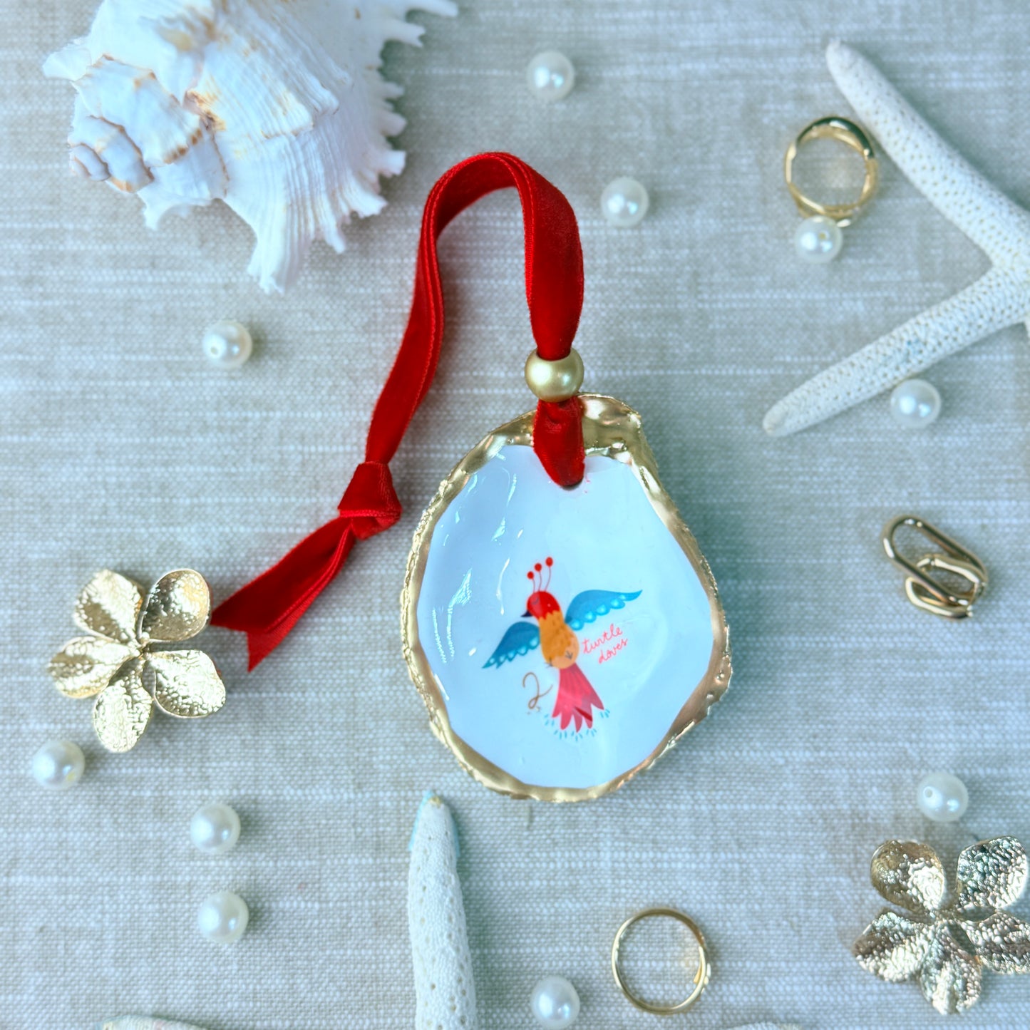 Decorative shell with a red ribbon and bird illustration on a textured surface with pearls and flowers.
