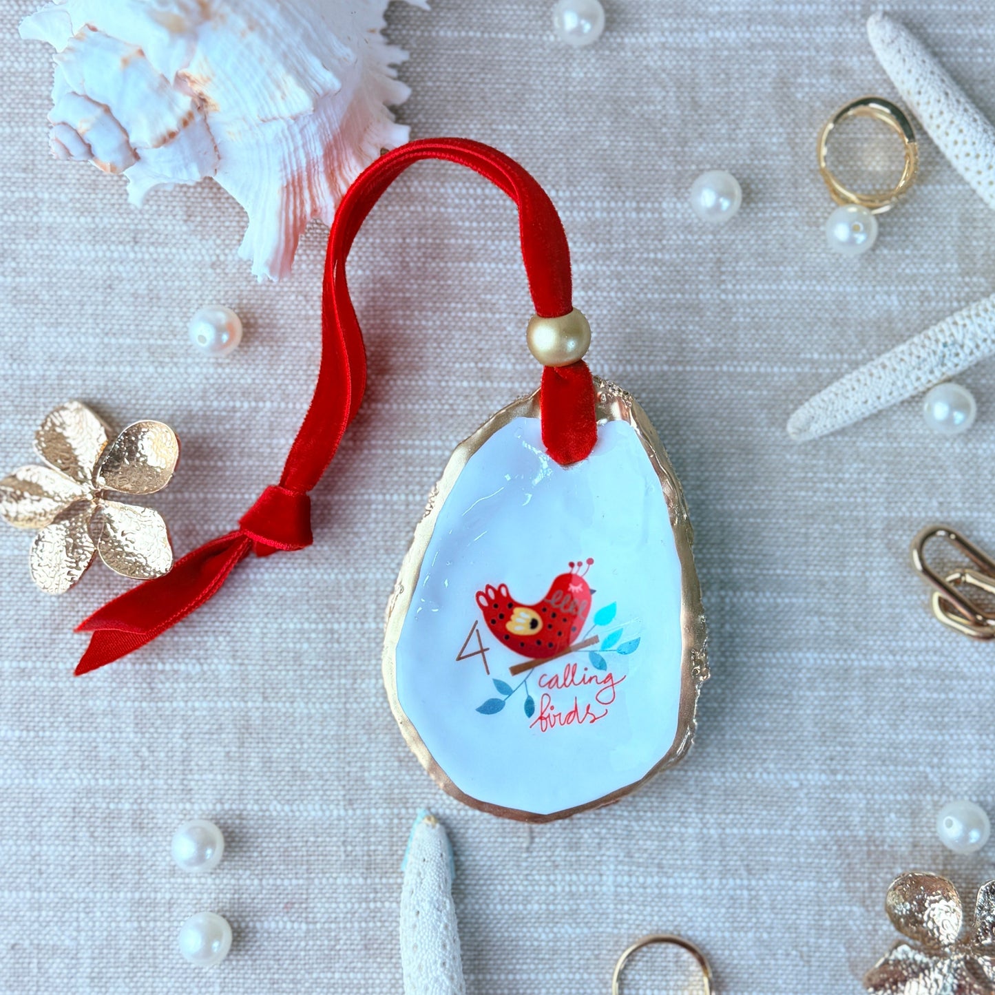 Decorative keychain with red bird design on a textured surface with shells and pearls.