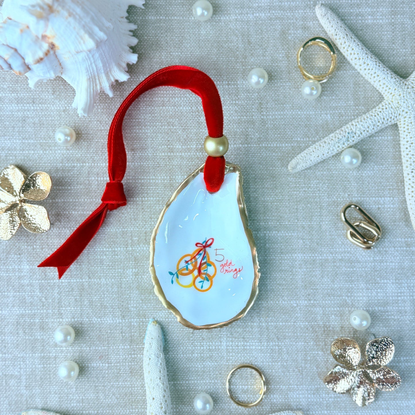 Decorative oyster shell with a red ribbon on a textured surface with starfish and pearls.