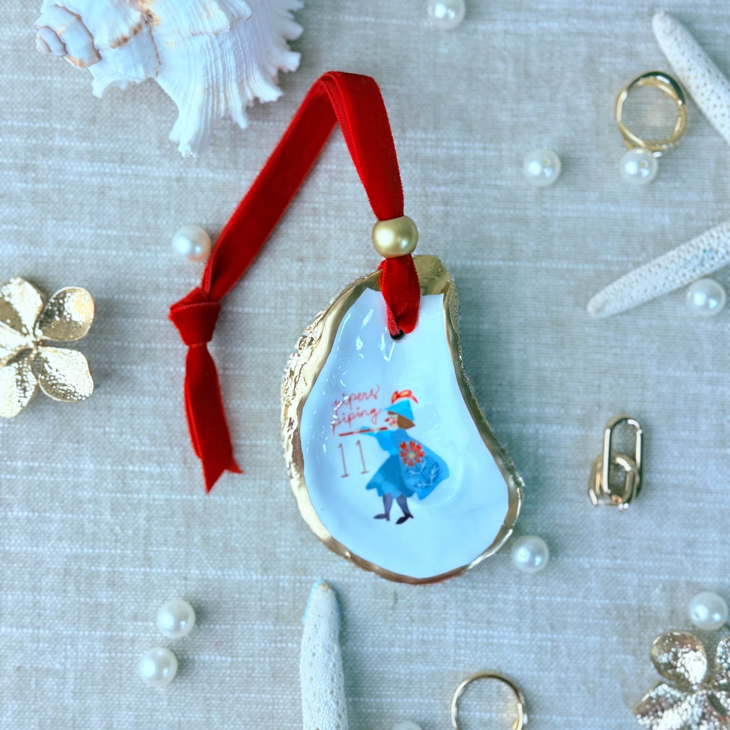 Decorative oyster shell with a painting of a woman and red ribbon, surrounded by pearls and starfish on a textured surface.