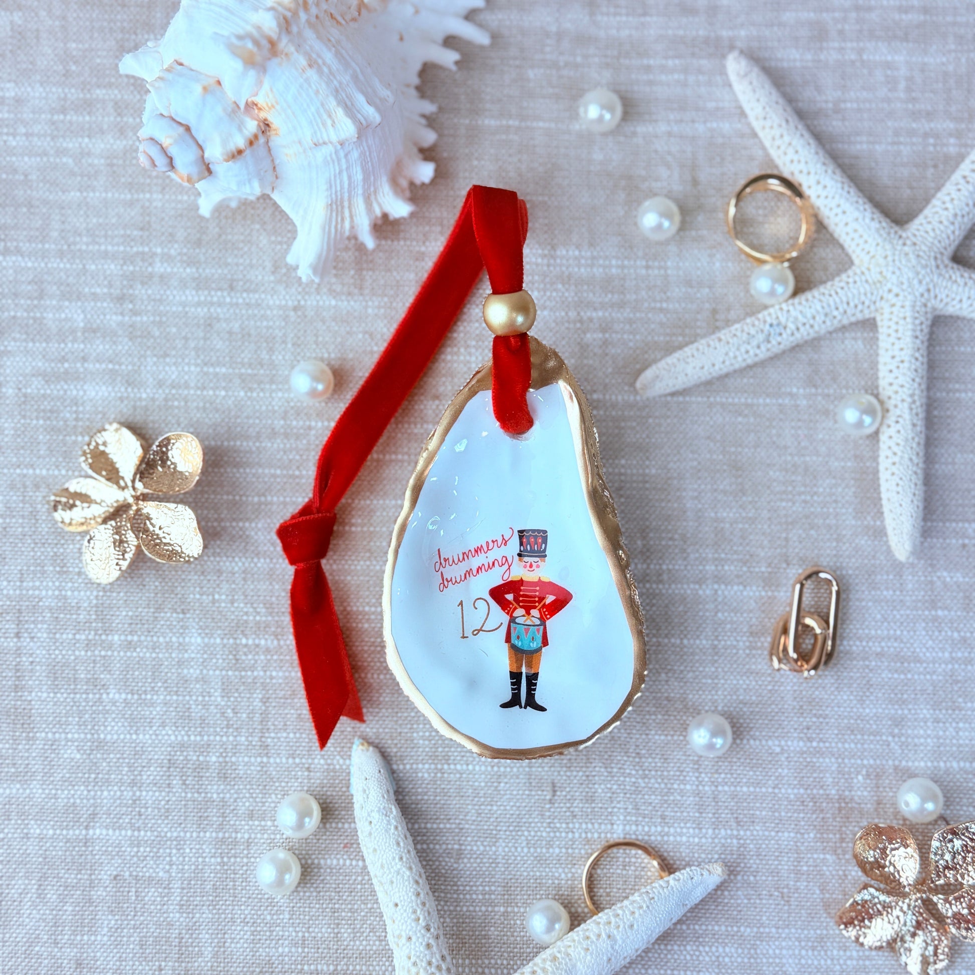 Decorative ornament with a red ribbon on a textured surface with shells and pearls.